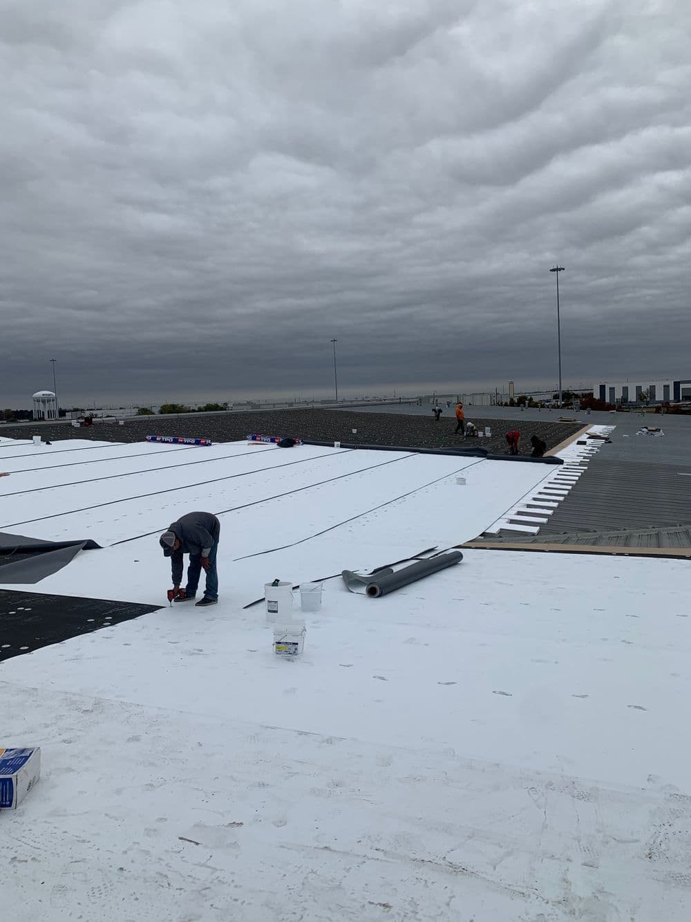Workers applying a white roofing system on a commercial building under a cloudy sky.