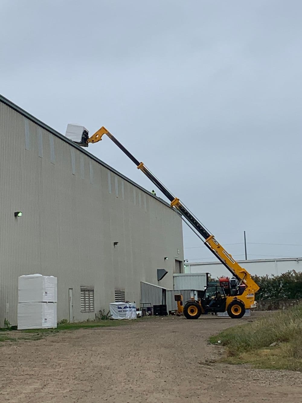 Worker using a telehandler to lift materials to the roof of a warehouse building.