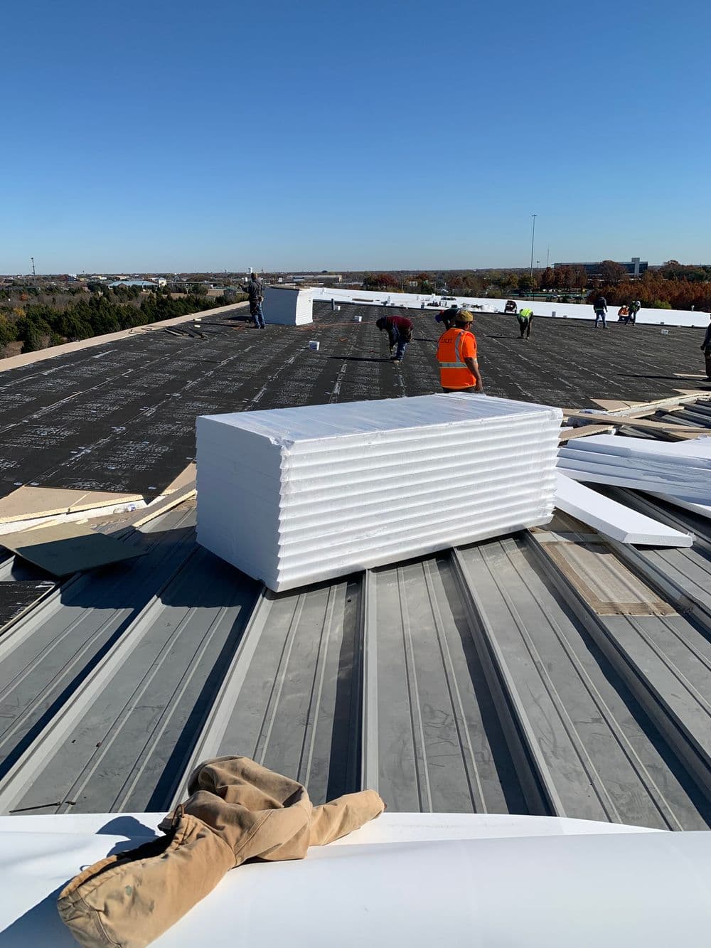 Construction workers installing roofing materials on a flat commercial roof on a clear day.