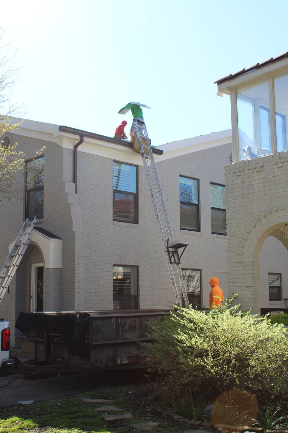 Workers repairing roof with ladder and truck in residential area on sunny day.