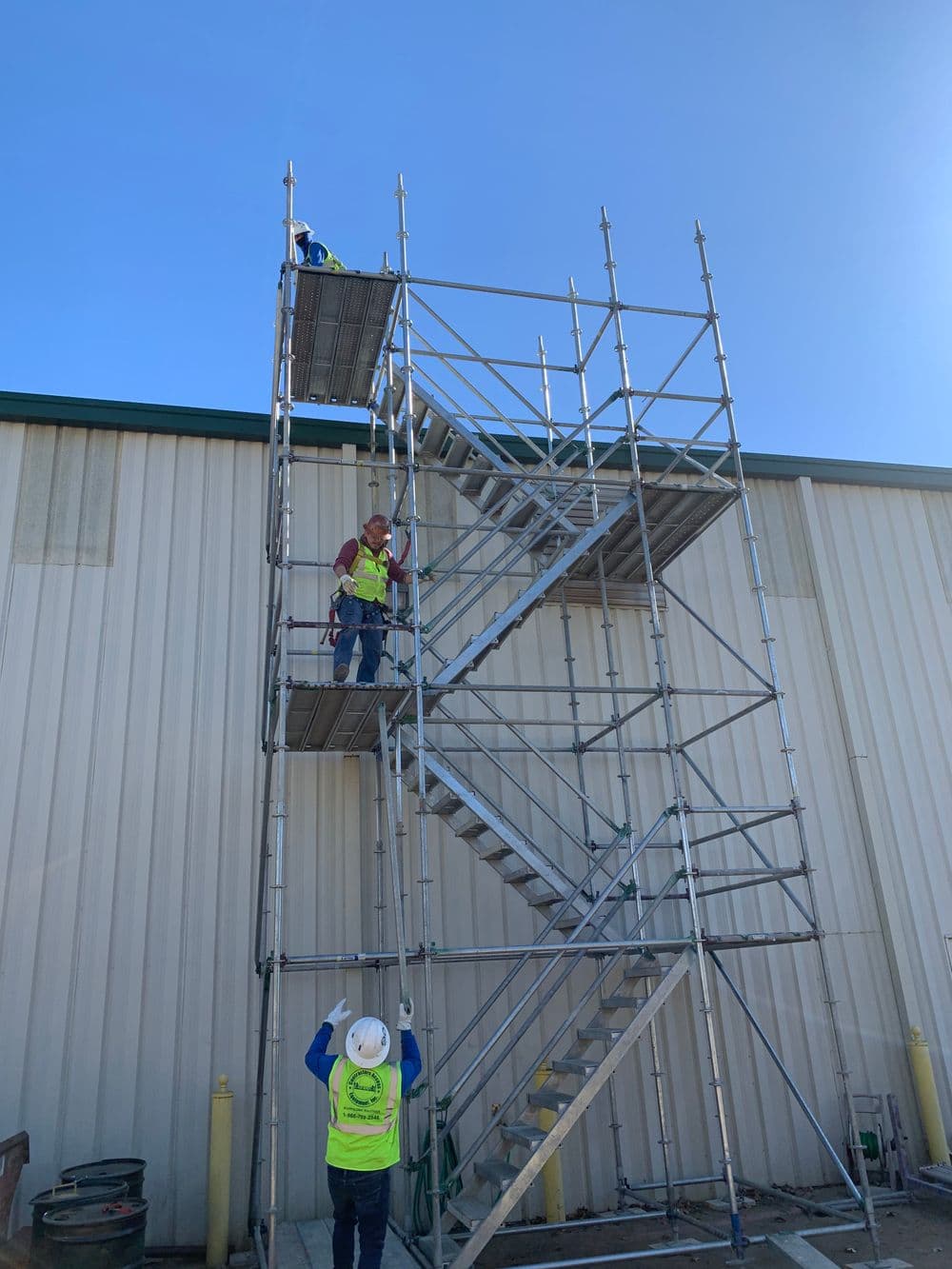 Construction workers assembling a tall scaffold with a clear blue sky in the background.
