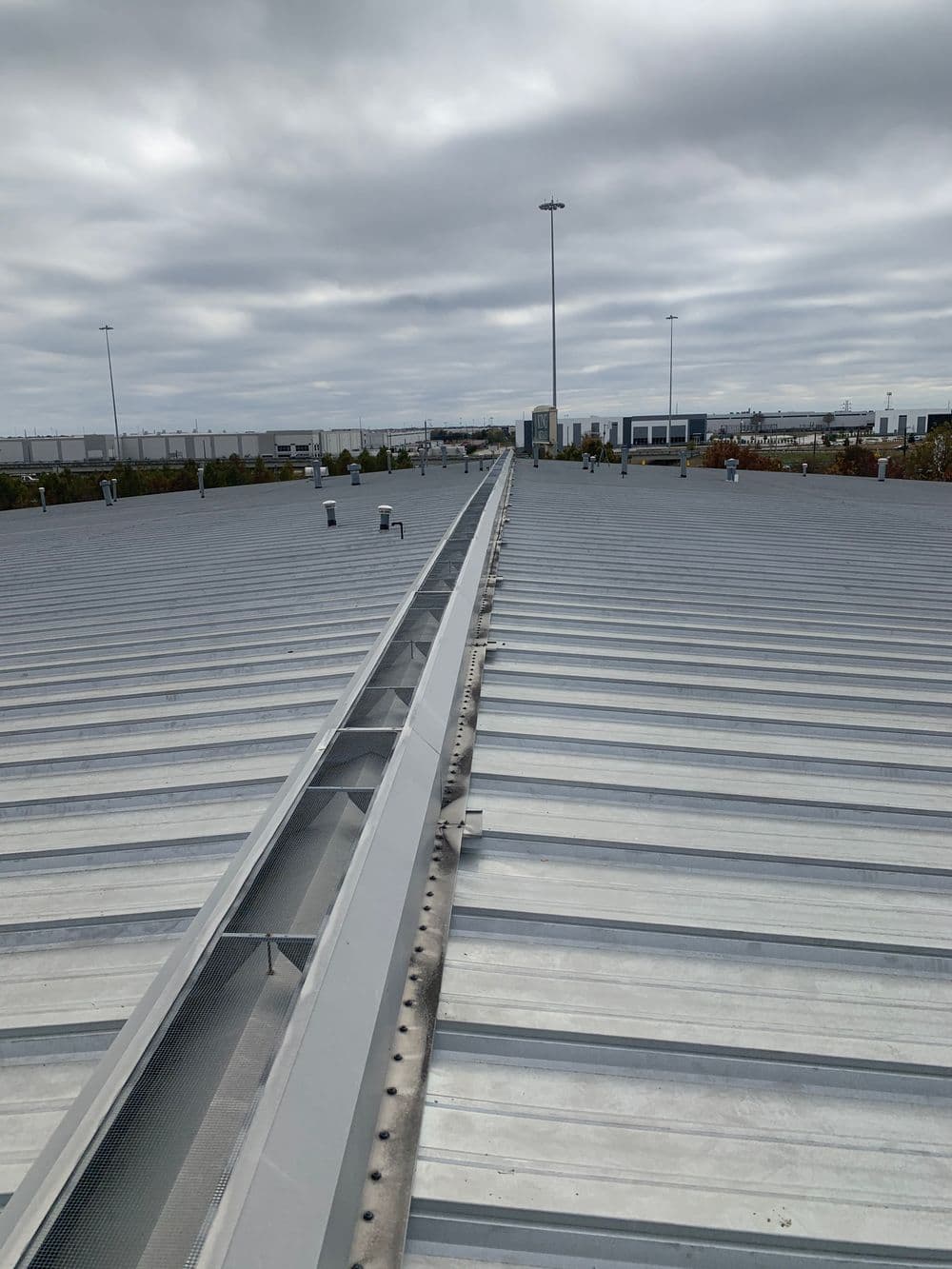 Steel roof with drainage system, viewed from the top under a cloudy sky.