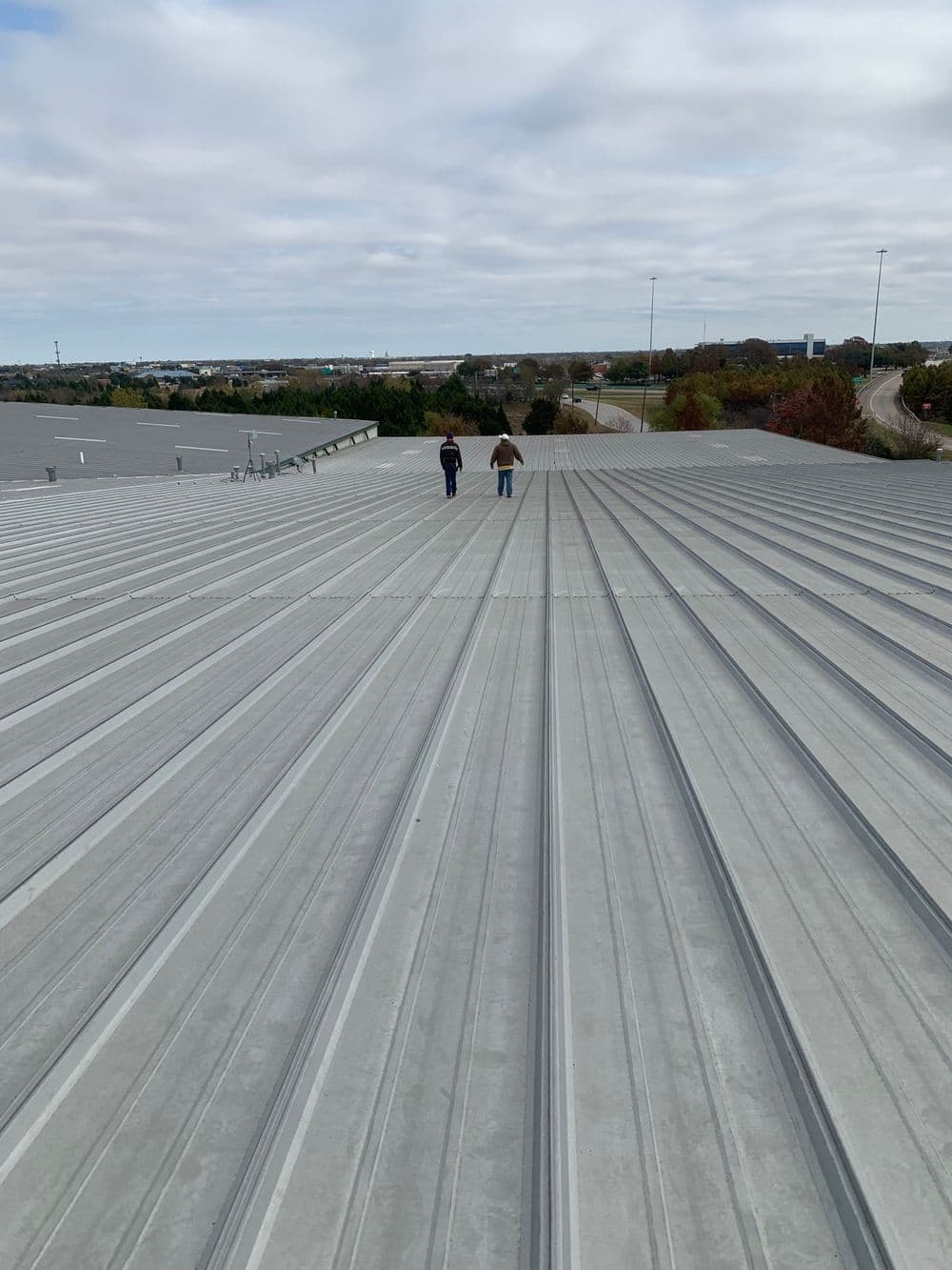 Two workers walking on a metal roof, overlooking a scenic landscape under a cloudy sky.
