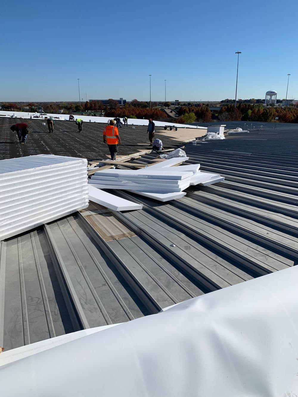 Workers installing insulation on a commercial roof with clear blue sky above.