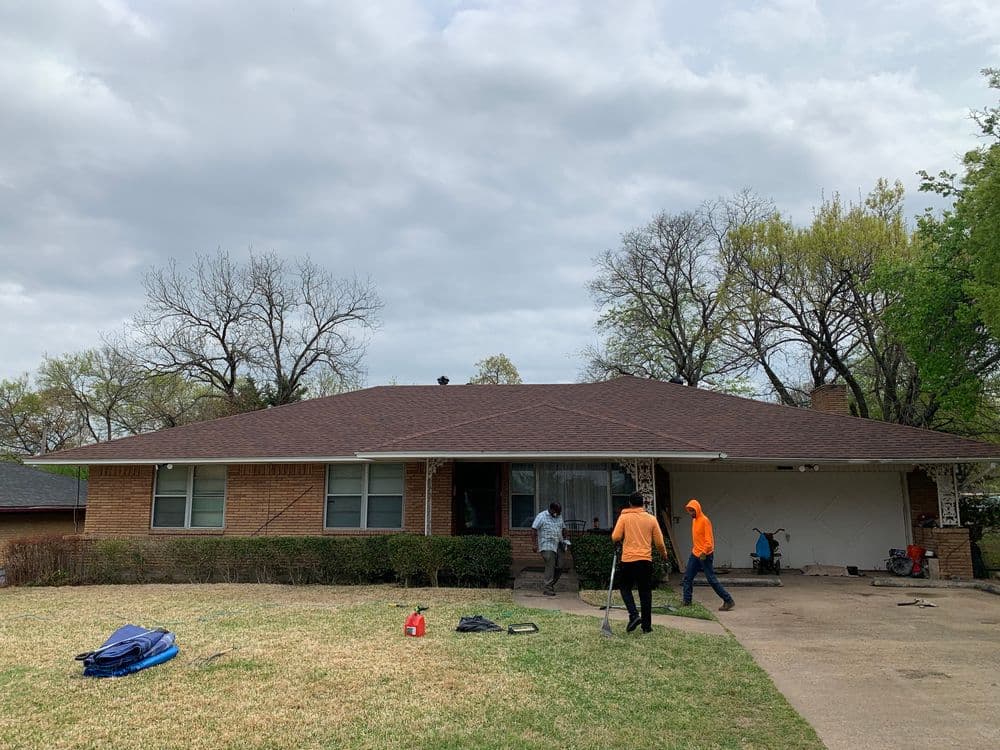 Home exterior with workers landscaping yard on cloudy day, showcasing brick facade and greenery.