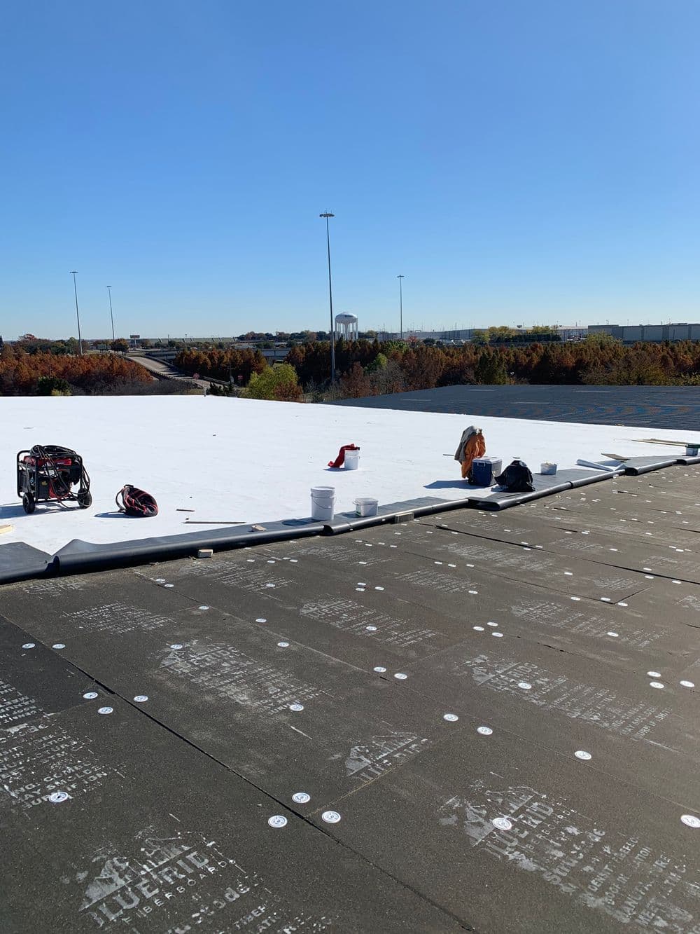 Roofing installation in progress with equipment on a commercial building rooftop under clear blue sky.