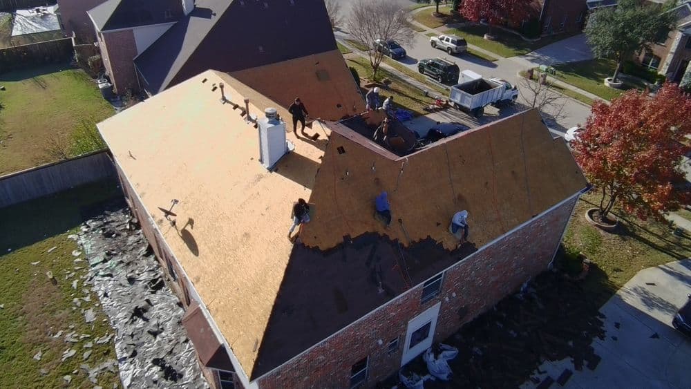 Workers installing a new roof on a residential home with stacked materials nearby.