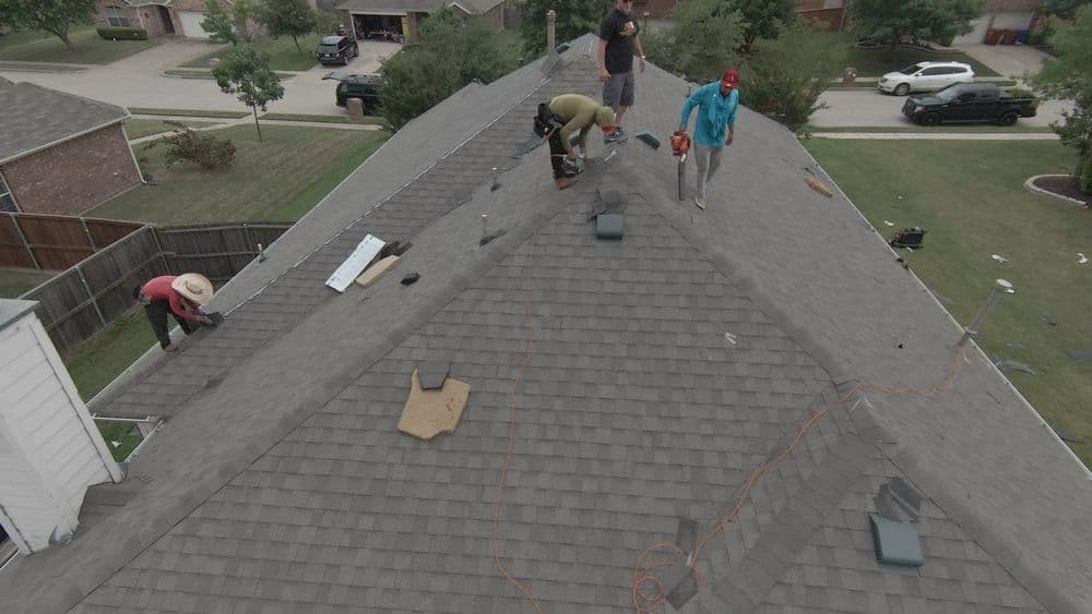 Workers installing shingles on a residential roof, showcasing roofing tools and materials.
