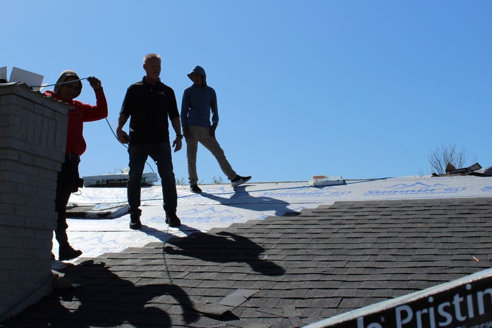 Roofing team working on a house, installing shingles under a clear blue sky.
