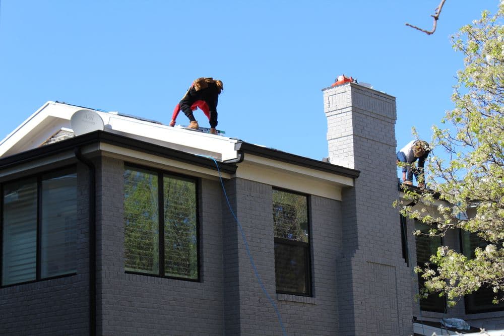 Roofing contractors repairing a home roof under clear blue skies.