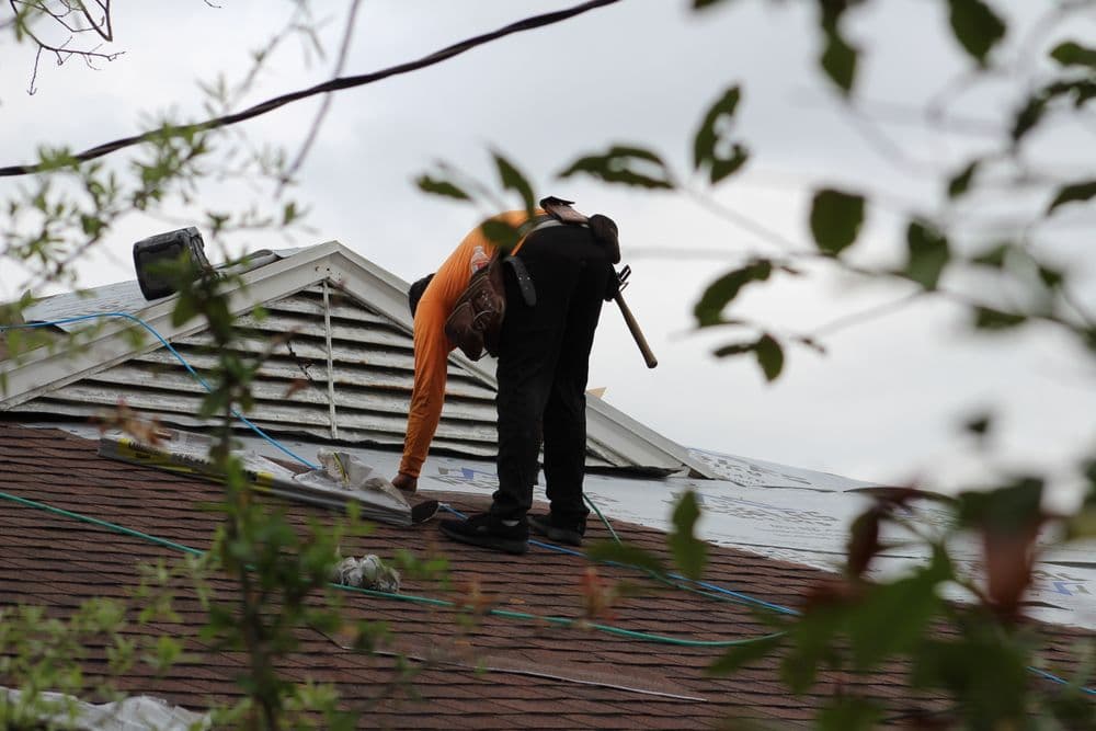 Roofers working on a house roof, installing materials with tools and safety equipment.