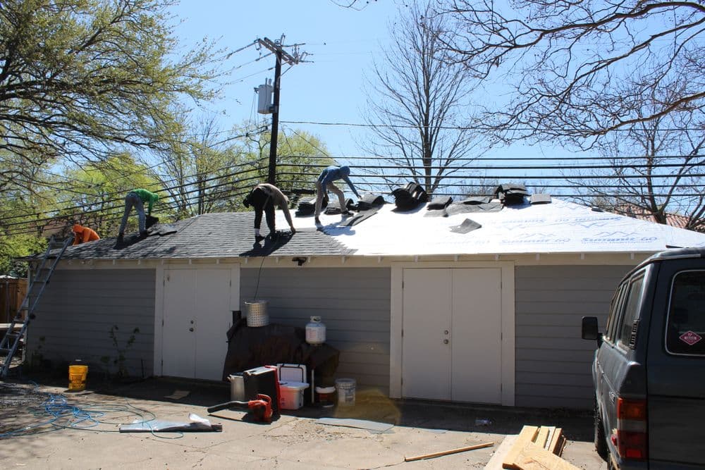 Workers installing a new roof on a residential building with tools and materials visible.