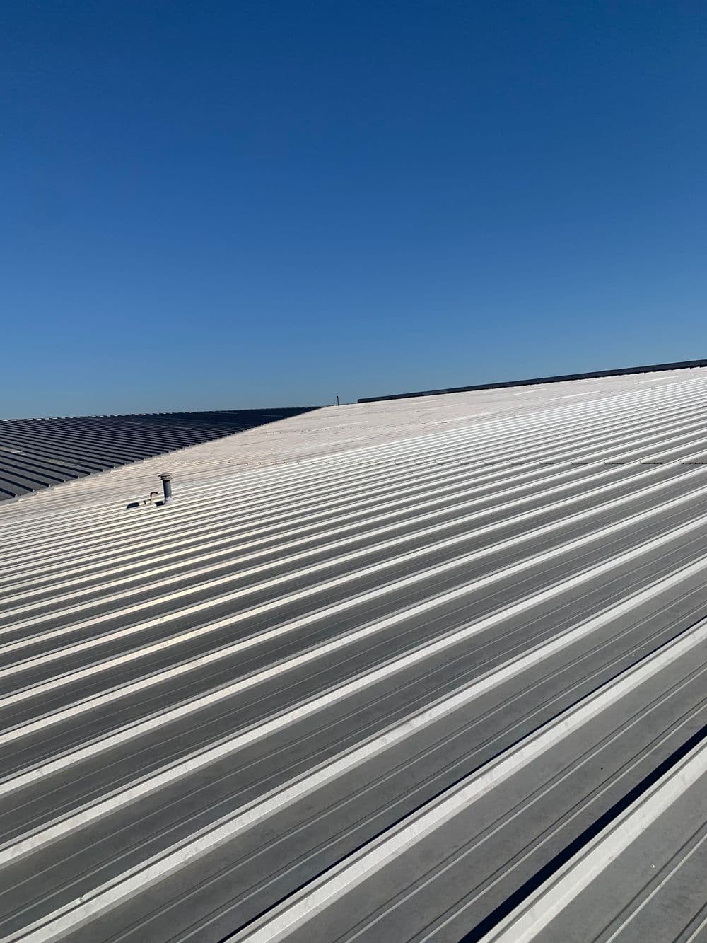 Metal roof with standing seams under clear blue sky, showcasing roofing installation work.