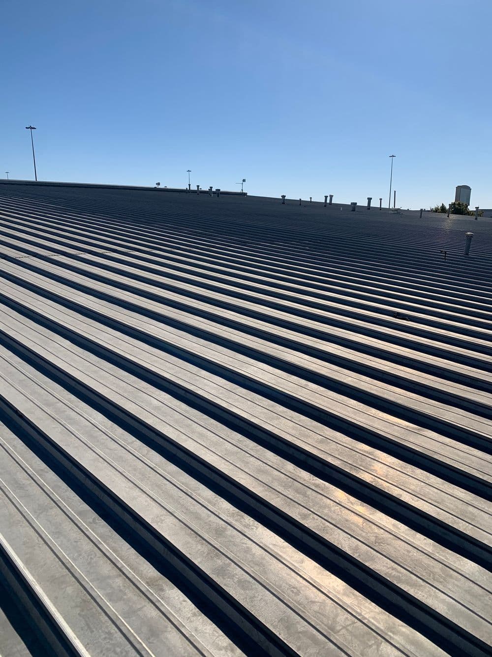 Metal roofing panels in sunlight on a commercial building under a clear blue sky.