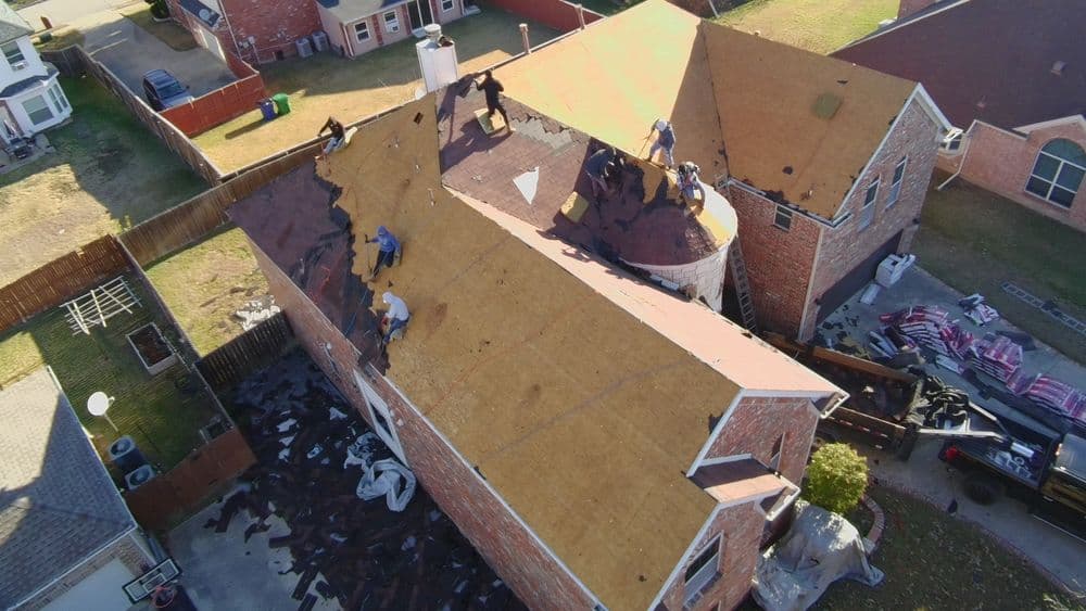 Roofing contractors replacing shingles on a residential home, aerial view of construction site.