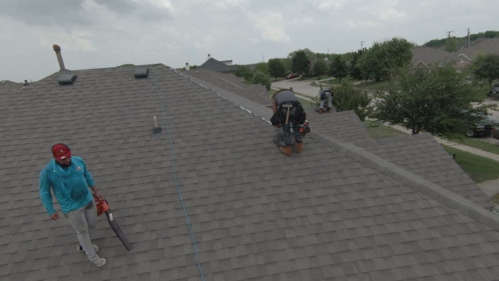 Roofing contractors installing shingles on a residential roof under cloudy skies.