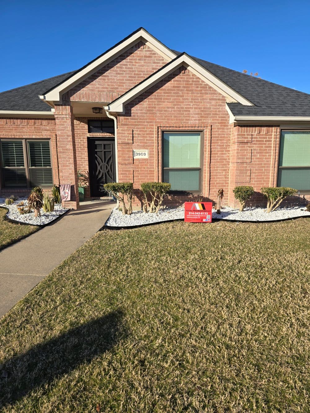 Brick house with manicured front yard, shrubs, and a for-sale sign in the lawn.