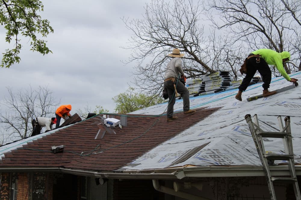 Roofers installing shingles on a residential roof under overcast skies.