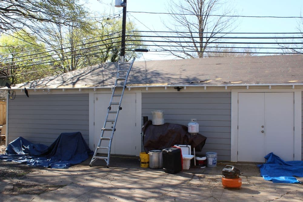 Garage exterior with ladder, tools, and construction materials on a sunny day.