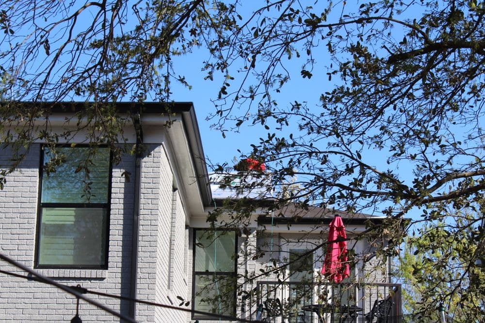 Modern house with a red umbrella on the balcony, framed by tree branches and clear blue sky.