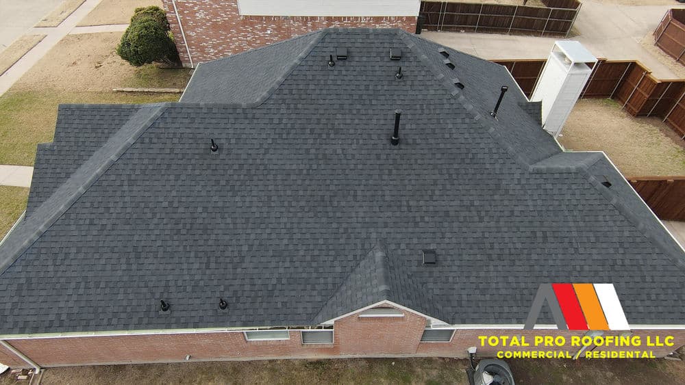 Aerial view of a residential roof with dark shingles, showcasing ventilation pipes and home structure.