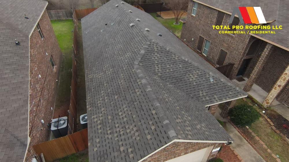 Aerial view of a residential roof showcasing gray shingles and neighboring homes. Total Pro Roofing logo.